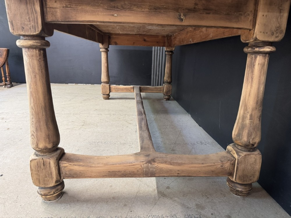 A large antique natural pine dining table featuring turned legs connected by a low H-stretcher and a solid plank top. View IX
