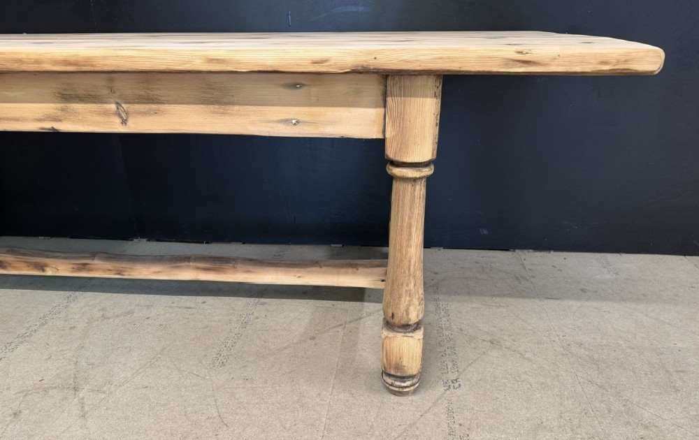 A large antique natural pine dining table featuring turned legs connected by a low H-stretcher and a solid plank top. View X