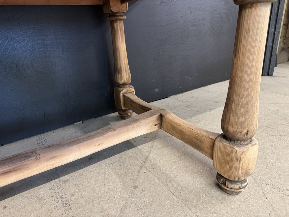 A large antique natural pine dining table featuring turned legs connected by a low H-stretcher and a solid plank top. View XII