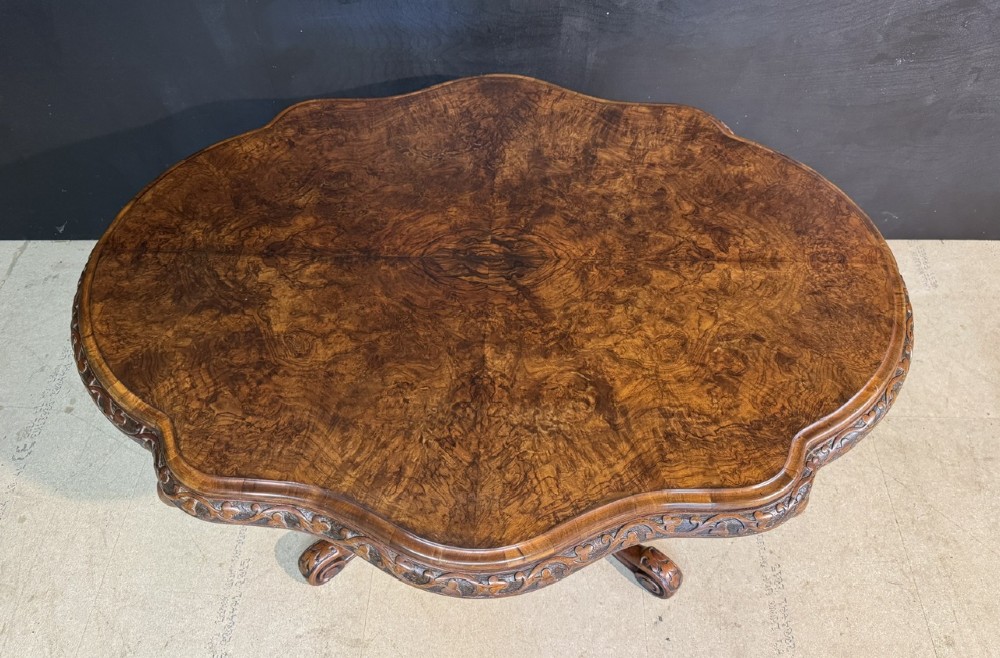 An antique burr walnut centre table featuring a shaped top, an intricately carved apron, and a quadruped pedestal base with scrolled feet. View II