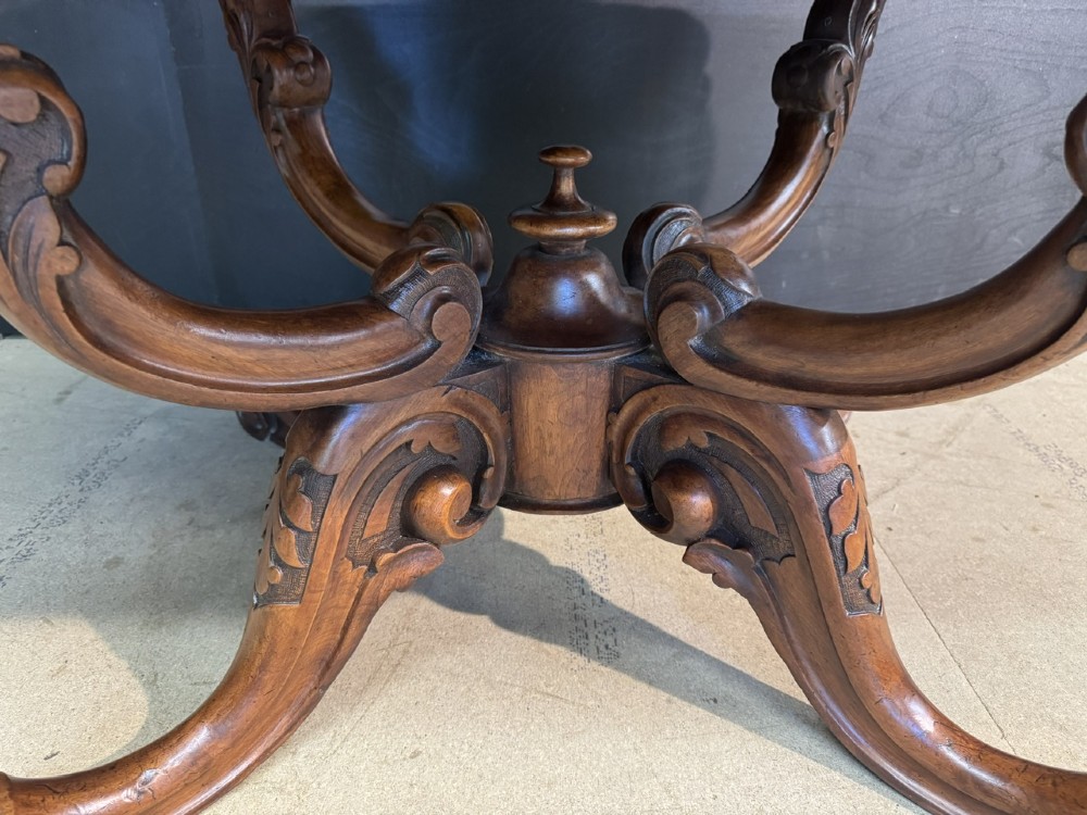 An antique burr walnut centre table featuring a shaped top, an intricately carved apron, and a quadruped pedestal base with scrolled feet. View IV