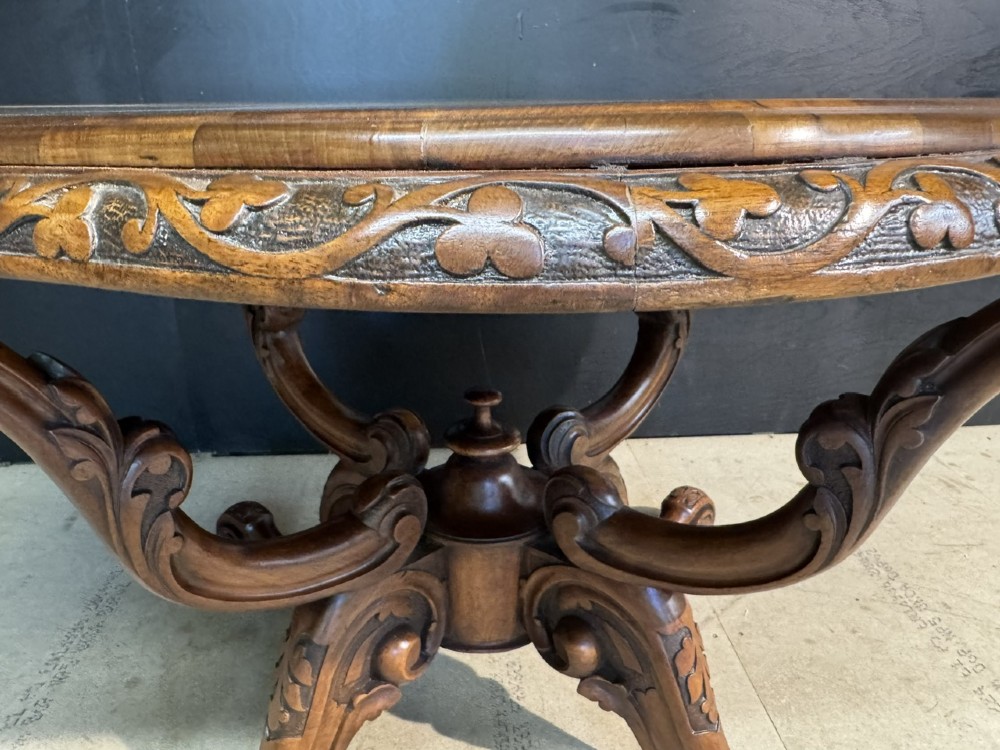An antique burr walnut centre table featuring a shaped top, an intricately carved apron, and a quadruped pedestal base with scrolled feet. View V