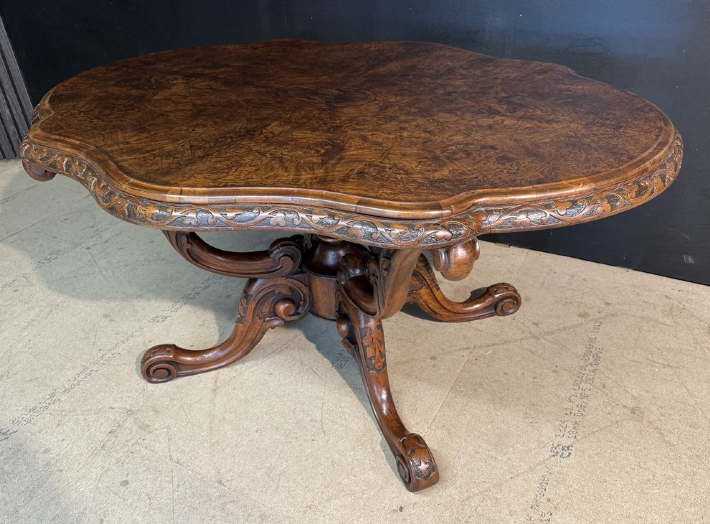 An antique burr walnut centre table featuring a shaped top, an intricately carved apron, and a quadruped pedestal base with scrolled feet. View VI