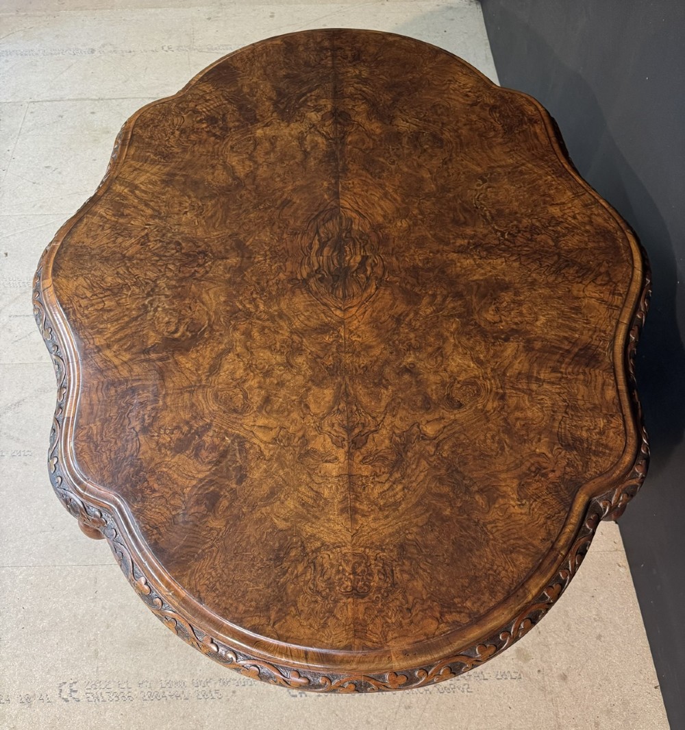 An antique burr walnut centre table featuring a shaped top, an intricately carved apron, and a quadruped pedestal base with scrolled feet. View VII