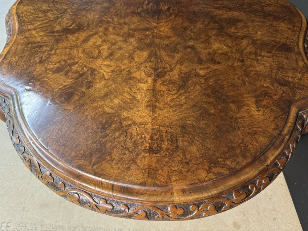 An antique burr walnut centre table featuring a shaped top, an intricately carved apron, and a quadruped pedestal base with scrolled feet. View VIII