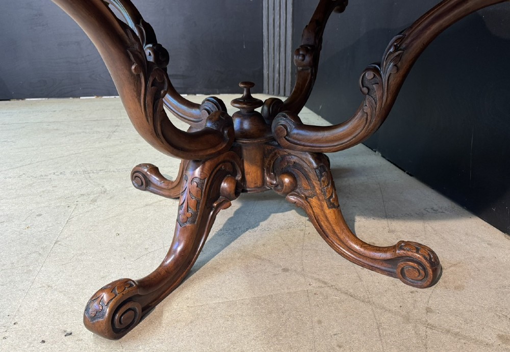 An antique burr walnut centre table featuring a shaped top, an intricately carved apron, and a quadruped pedestal base with scrolled feet. View IX