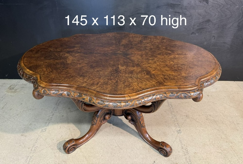 An antique burr walnut centre table featuring a shaped top, an intricately carved apron, and a quadruped pedestal base with scrolled feet. View X