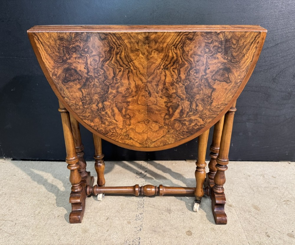 An antique Victorian burr walnut Sutherland table featuring an oval drop-leaf top, turned support legs, and small castors. View II