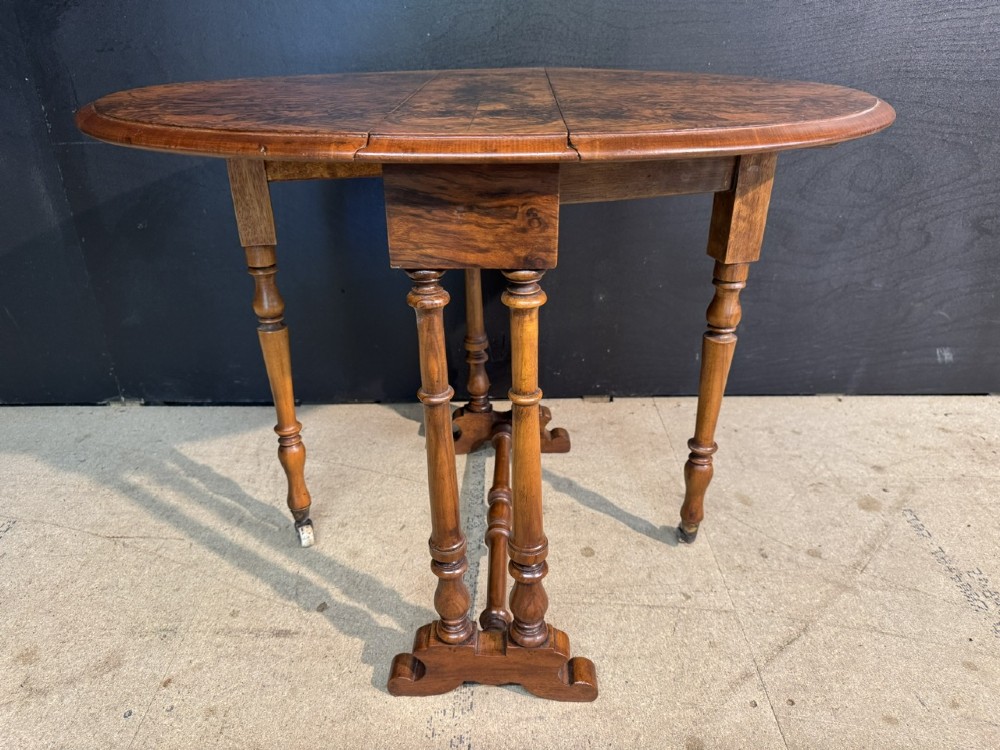 An antique Victorian burr walnut Sutherland table featuring an oval drop-leaf top, turned support legs, and small castors. View V