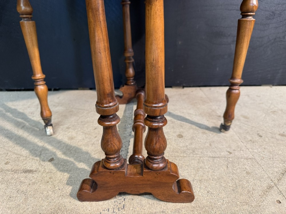 An antique Victorian burr walnut Sutherland table featuring an oval drop-leaf top, turned support legs, and small castors. View VI
