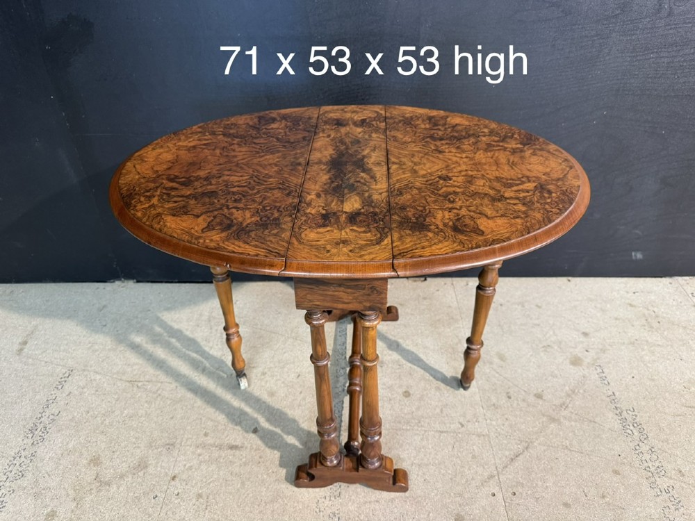 An antique Victorian burr walnut Sutherland table featuring an oval drop-leaf top, turned support legs, and small castors. View VIII