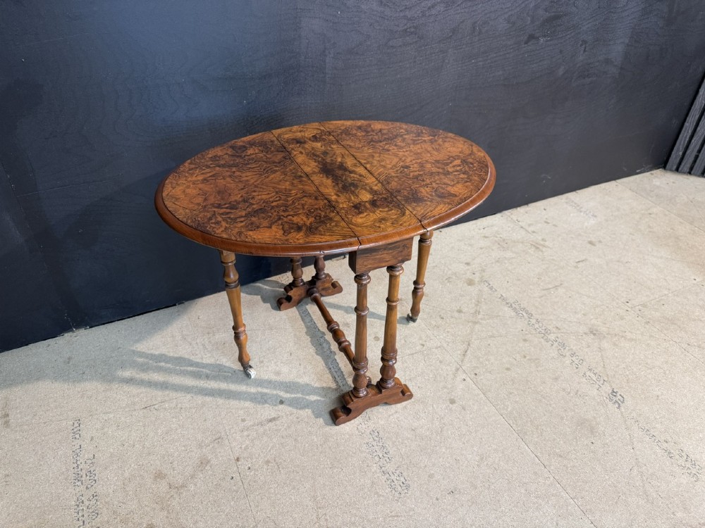 An antique Victorian burr walnut Sutherland table featuring an oval drop-leaf top, turned support legs, and small castors. View IX