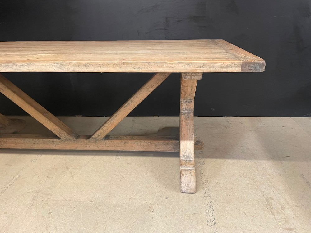 A large, pale pine farmhouse dining table featuring a solid timber top and a sturdy trestle-style base with diagonal bracing. View VII