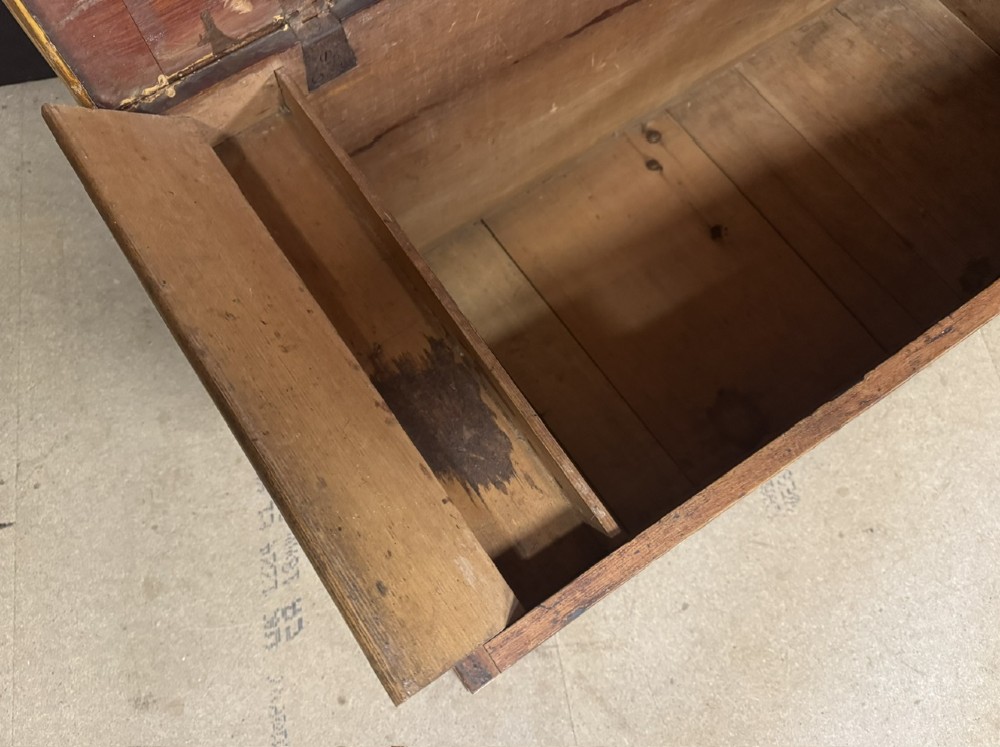 A low rectangular antique pine chest featuring prominent wood graining, a hinged flat lid, central keyhole, and a solid plinth base. View VI