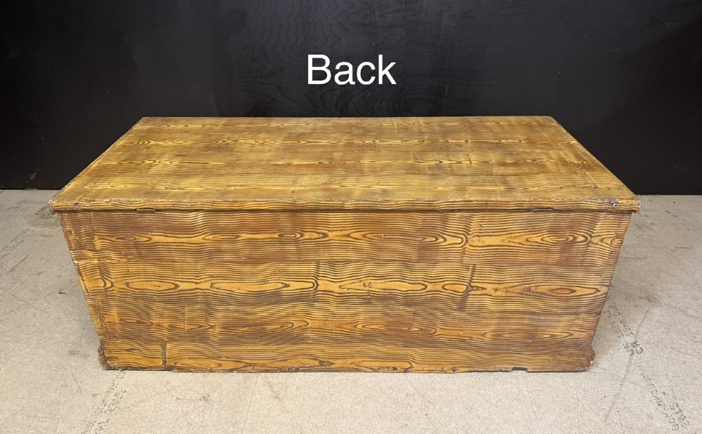 A low rectangular antique pine chest featuring prominent wood graining, a hinged flat lid, central keyhole, and a solid plinth base. View VIII