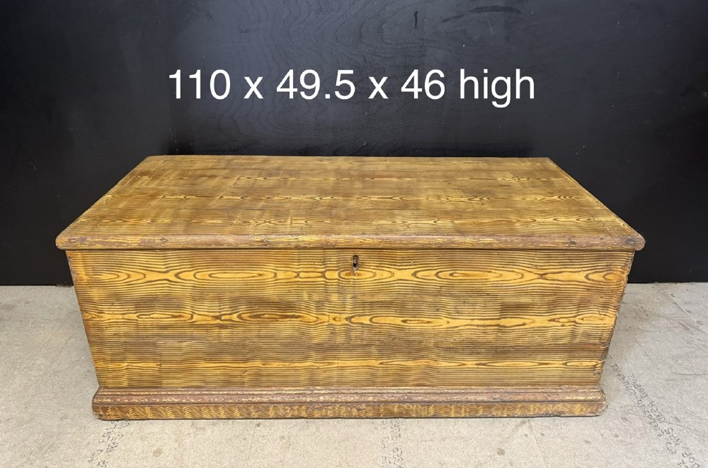 A low rectangular antique pine chest featuring prominent wood graining, a hinged flat lid, central keyhole, and a solid plinth base. View IX