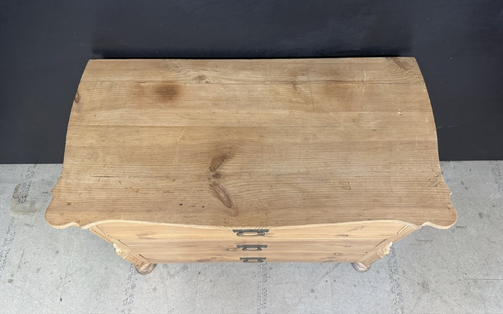 A three-drawer stripped pine chest of drawers featuring carved side corbels, brass drop handles, and turned bun feet. View VIII