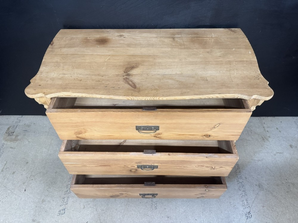 A three-drawer stripped pine chest of drawers featuring carved side corbels, brass drop handles, and turned bun feet. View IX