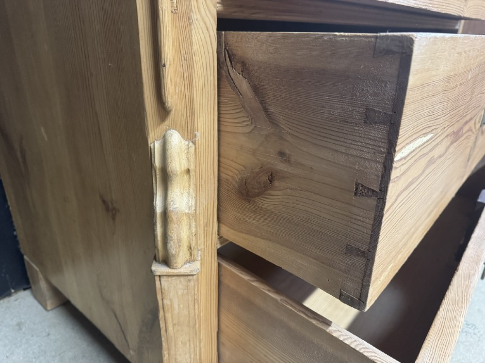 A three-drawer stripped pine chest of drawers featuring carved side corbels, brass drop handles, and turned bun feet. View X