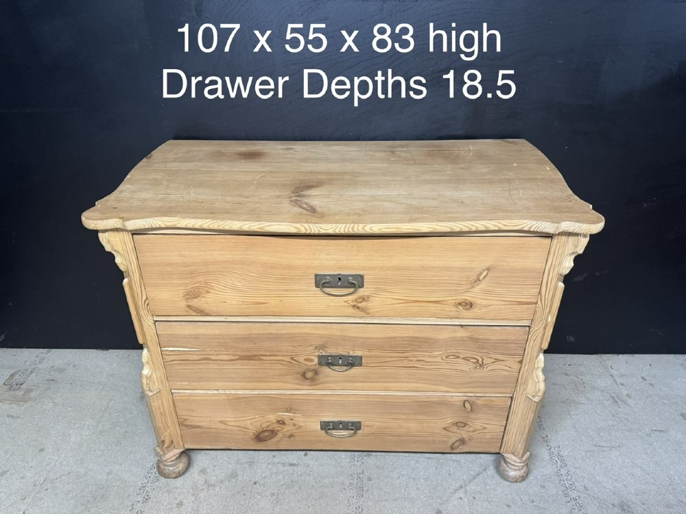 A three-drawer stripped pine chest of drawers featuring carved side corbels, brass drop handles, and turned bun feet. View XII