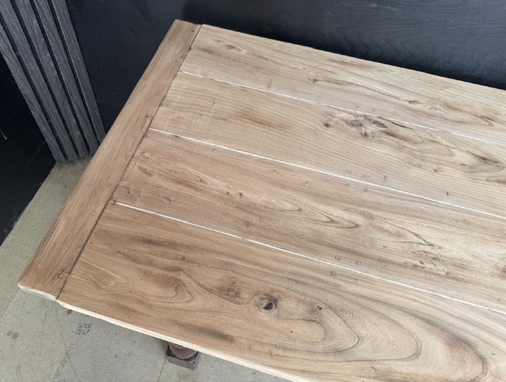 A rustic wooden dining table with a natural scrubbed timber top, carved apron frieze, turned legs, and a floor-level H-stretcher. View VI