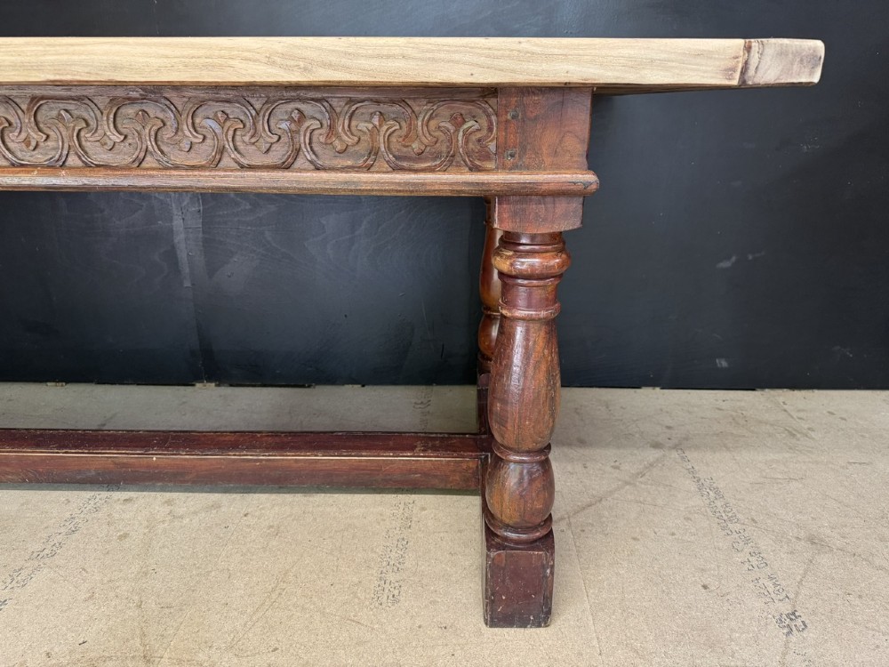 A rustic wooden dining table with a natural scrubbed timber top, carved apron frieze, turned legs, and a floor-level H-stretcher. View VIII