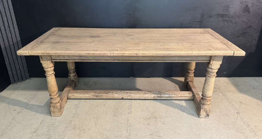 A rectangular bleached oak farmhouse dining table with turned legs, breadboard ends, and a low central stretcher base.