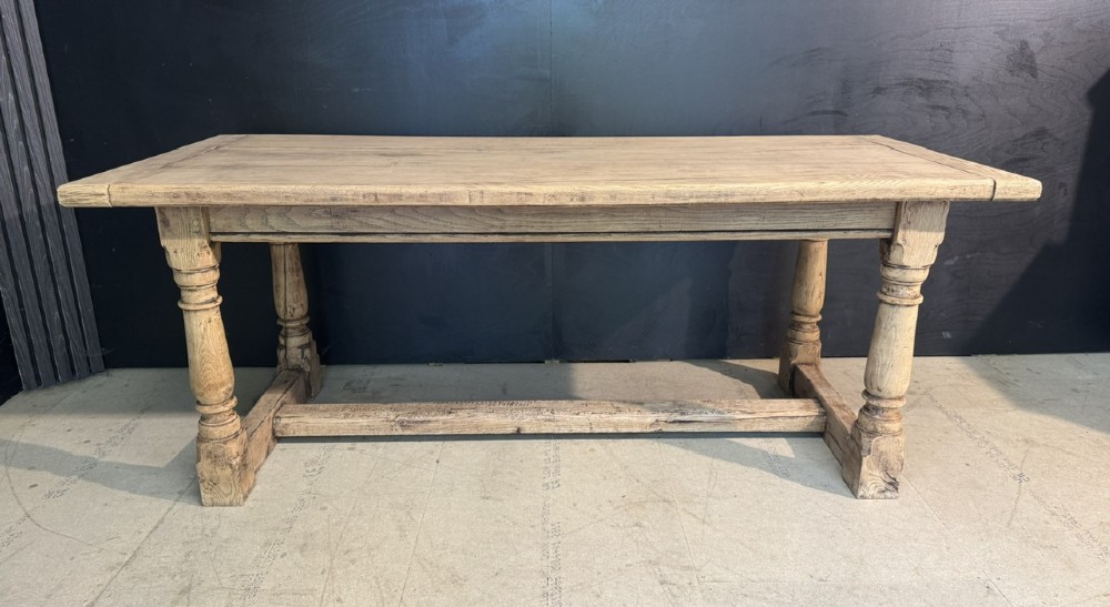 A rectangular bleached oak farmhouse dining table with turned legs, breadboard ends, and a low central stretcher base. View II