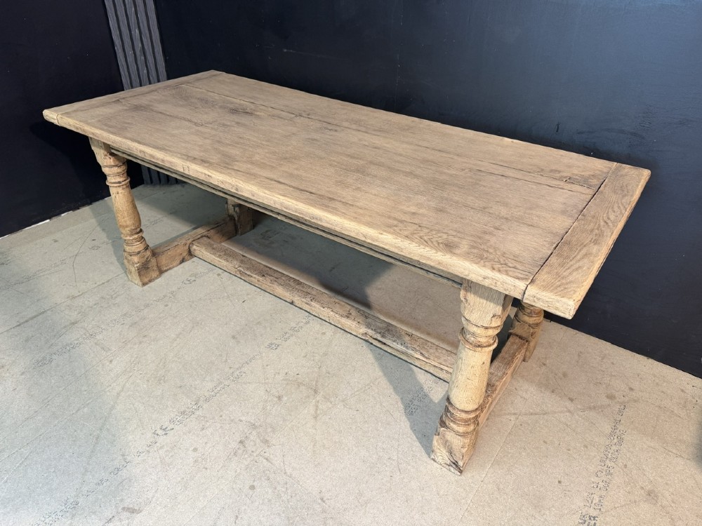 A rectangular bleached oak farmhouse dining table with turned legs, breadboard ends, and a low central stretcher base. View III