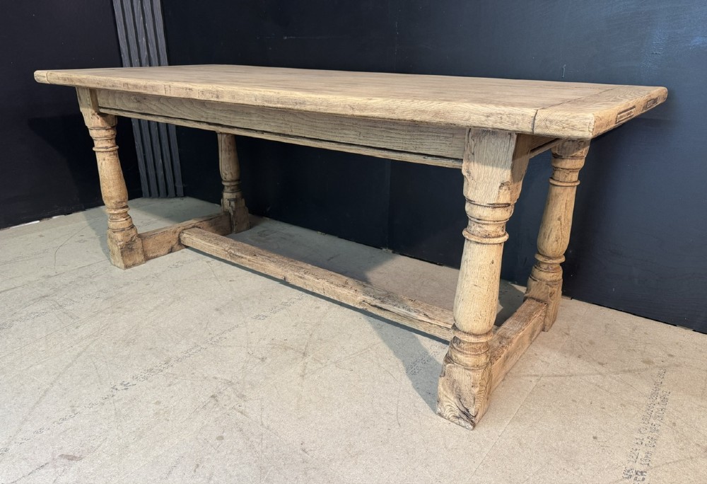 A rectangular bleached oak farmhouse dining table with turned legs, breadboard ends, and a low central stretcher base. View V