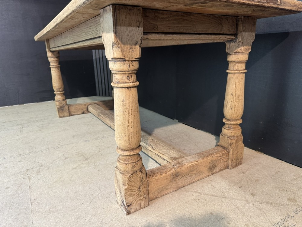 A rectangular bleached oak farmhouse dining table with turned legs, breadboard ends, and a low central stretcher base. View VI