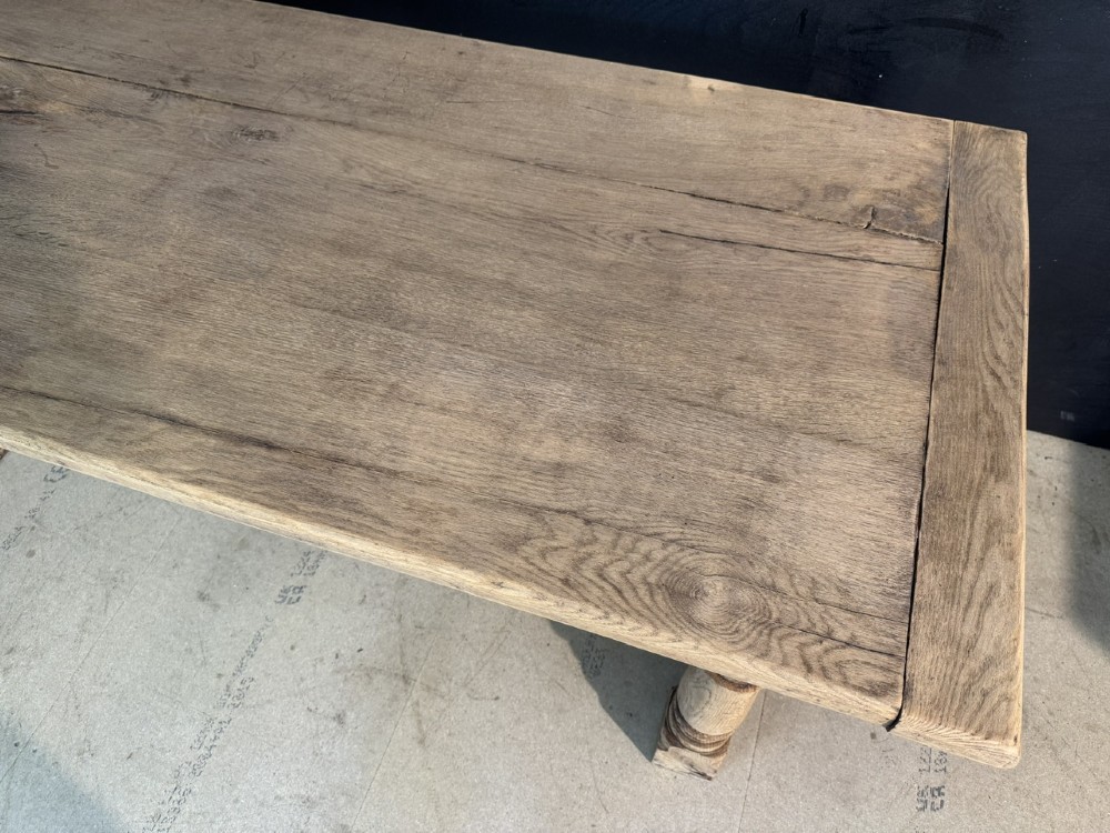 A rectangular bleached oak farmhouse dining table with turned legs, breadboard ends, and a low central stretcher base. View XII
