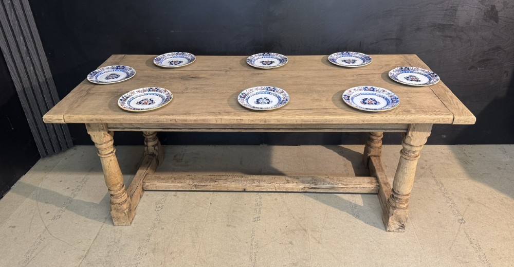 A rectangular bleached oak farmhouse dining table with turned legs, breadboard ends, and a low central stretcher base. View XV