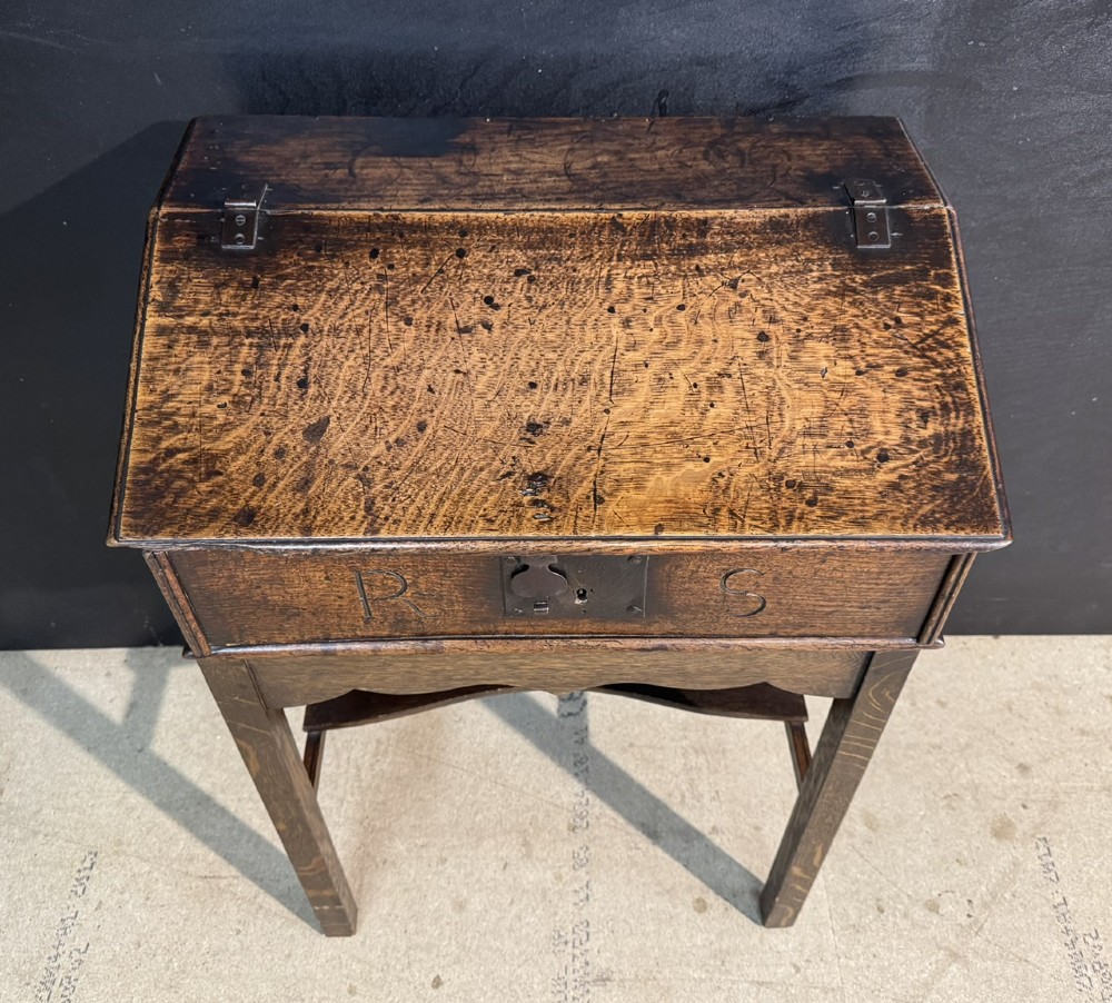 A 17th-century dark oak writing slope box on a wooden stand, featuring carved initials R S and a central iron lock plate. View II