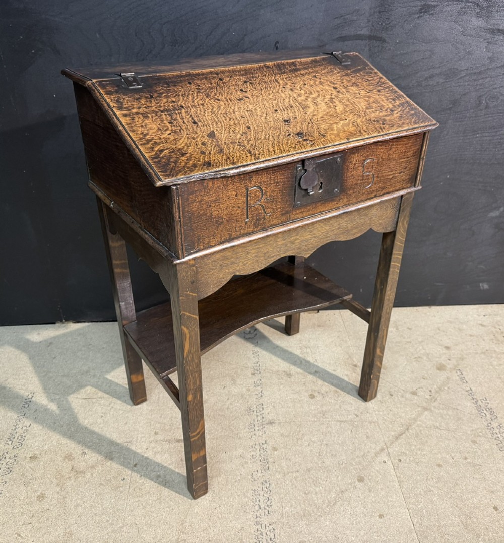 A 17th-century dark oak writing slope box on a wooden stand, featuring carved initials R S and a central iron lock plate. View III