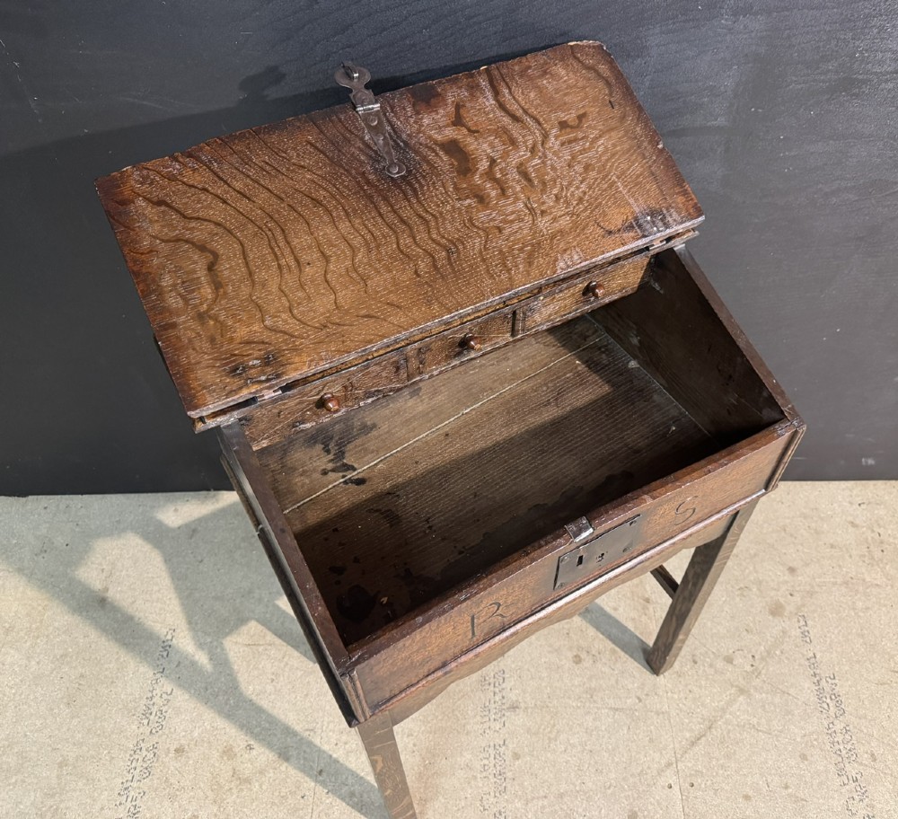 A 17th-century dark oak writing slope box on a wooden stand, featuring carved initials R S and a central iron lock plate. View IV