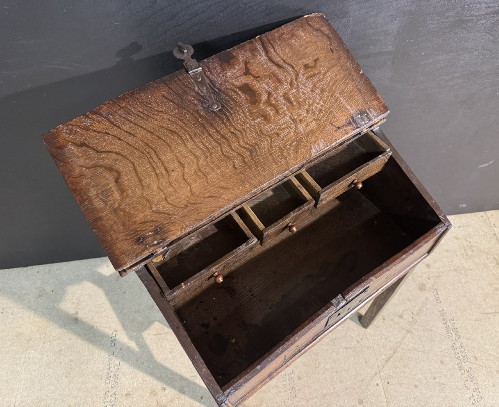 A 17th-century dark oak writing slope box on a wooden stand, featuring carved initials R S and a central iron lock plate. View V