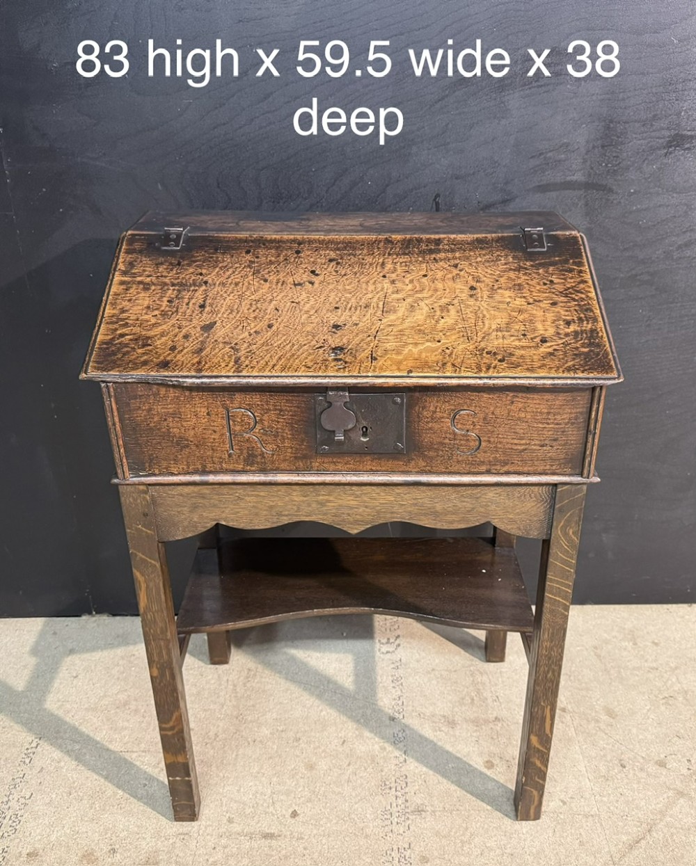 A 17th-century dark oak writing slope box on a wooden stand, featuring carved initials R S and a central iron lock plate. View XI