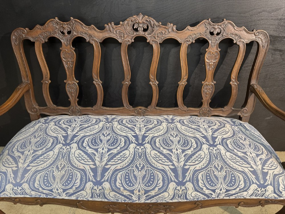 A carved walnut three-seater Rococo Revival settee featuring an openwork backrest with vertical splats and a blue and white patterned upholstered seat. View II