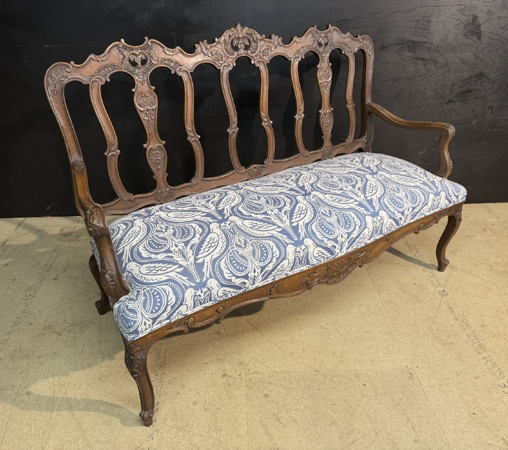 A carved walnut three-seater Rococo Revival settee featuring an openwork backrest with vertical splats and a blue and white patterned upholstered seat. View V
