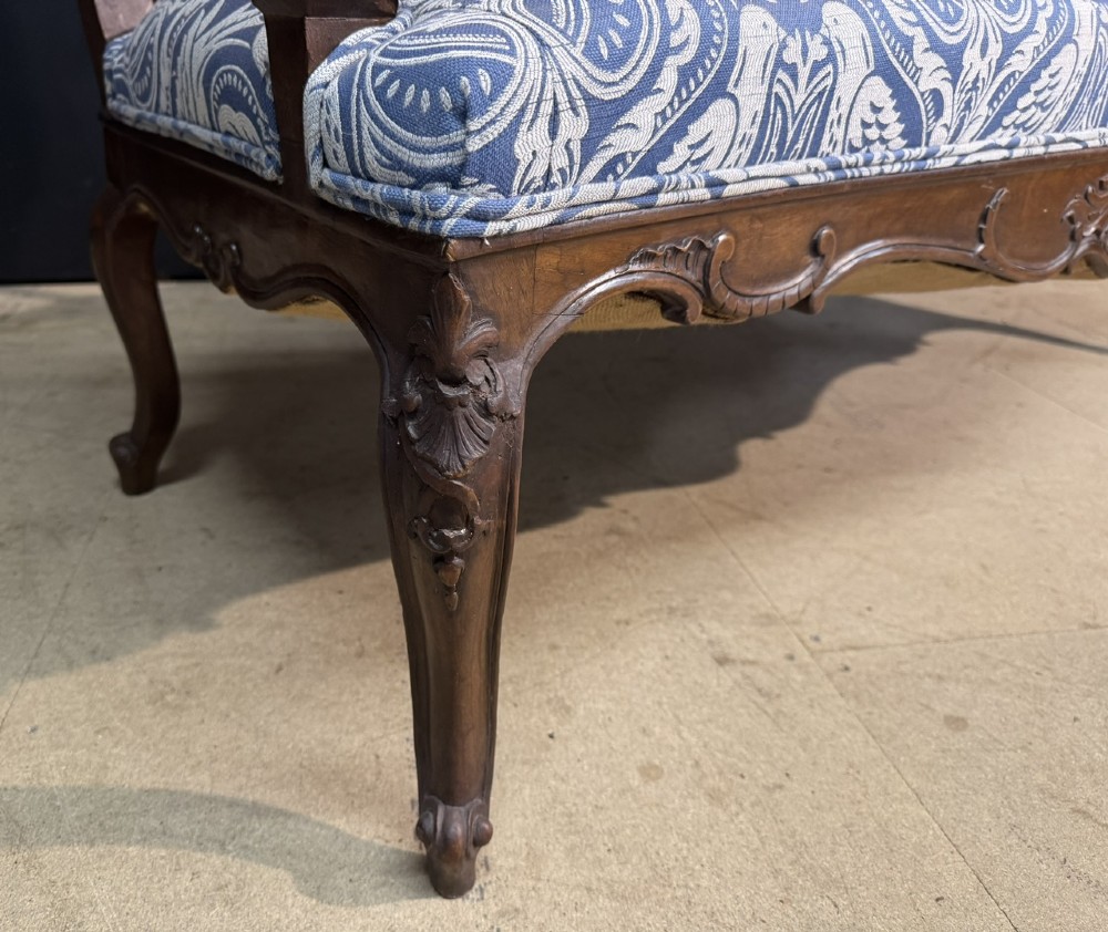A carved walnut three-seater Rococo Revival settee featuring an openwork backrest with vertical splats and a blue and white patterned upholstered seat. View VI