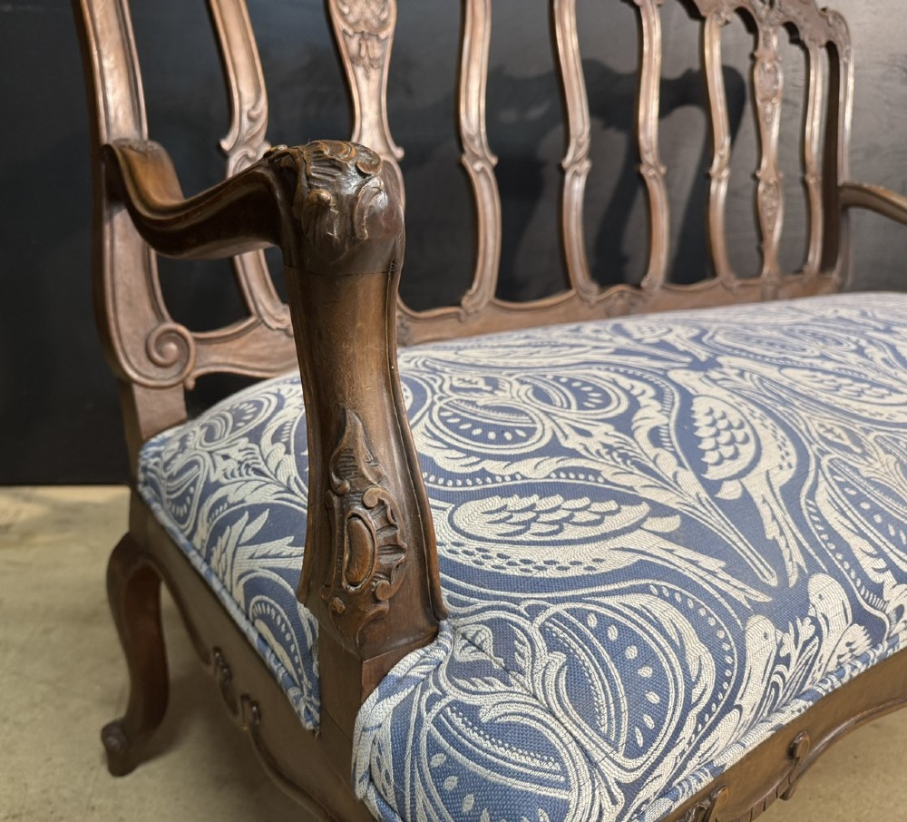 A carved walnut three-seater Rococo Revival settee featuring an openwork backrest with vertical splats and a blue and white patterned upholstered seat. View VII