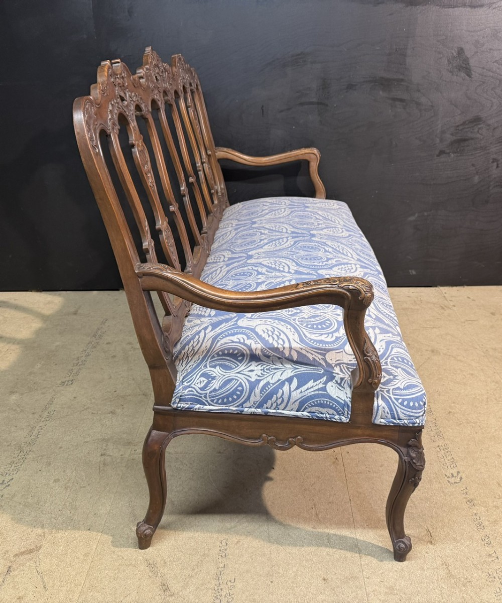 A carved walnut three-seater Rococo Revival settee featuring an openwork backrest with vertical splats and a blue and white patterned upholstered seat. View VIII