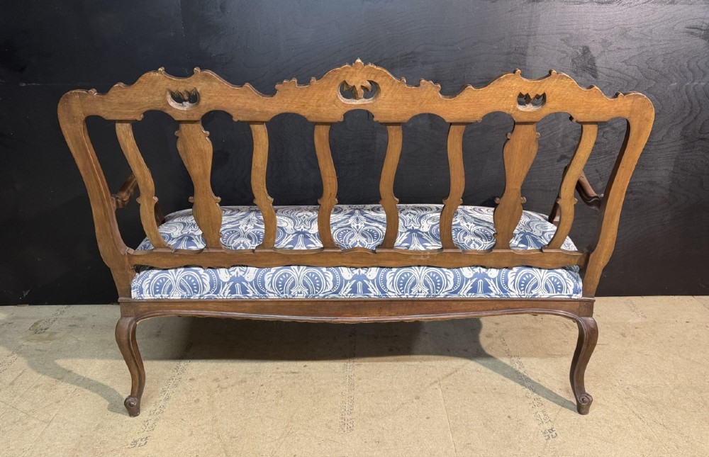 A carved walnut three-seater Rococo Revival settee featuring an openwork backrest with vertical splats and a blue and white patterned upholstered seat. View IX