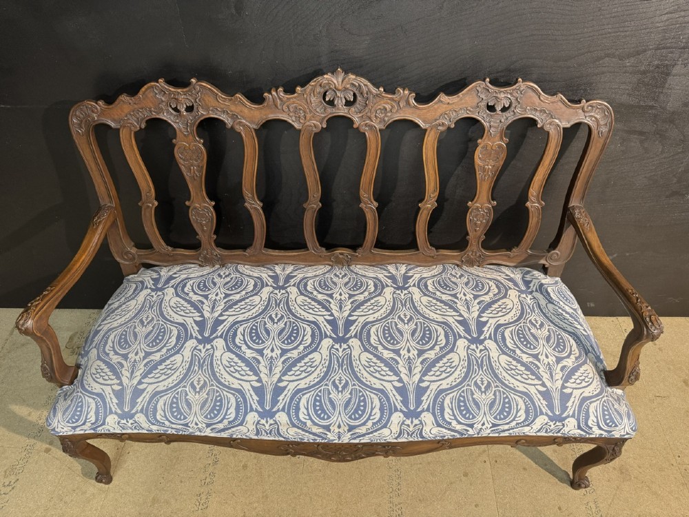 A carved walnut three-seater Rococo Revival settee featuring an openwork backrest with vertical splats and a blue and white patterned upholstered seat. View XIV