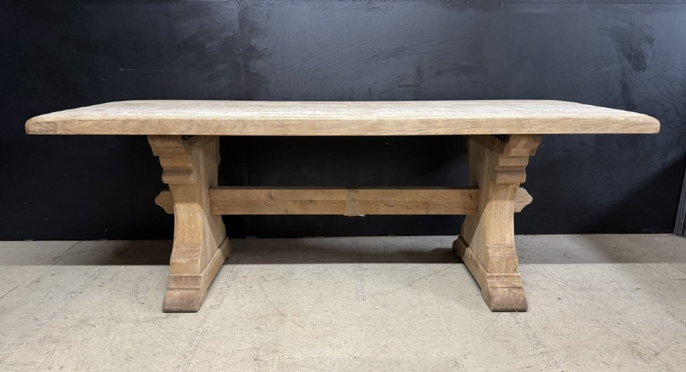 A rectangular bleached oak farmhouse dining table featuring a thick timber top supported by carved trestle legs and a central stretcher. View II