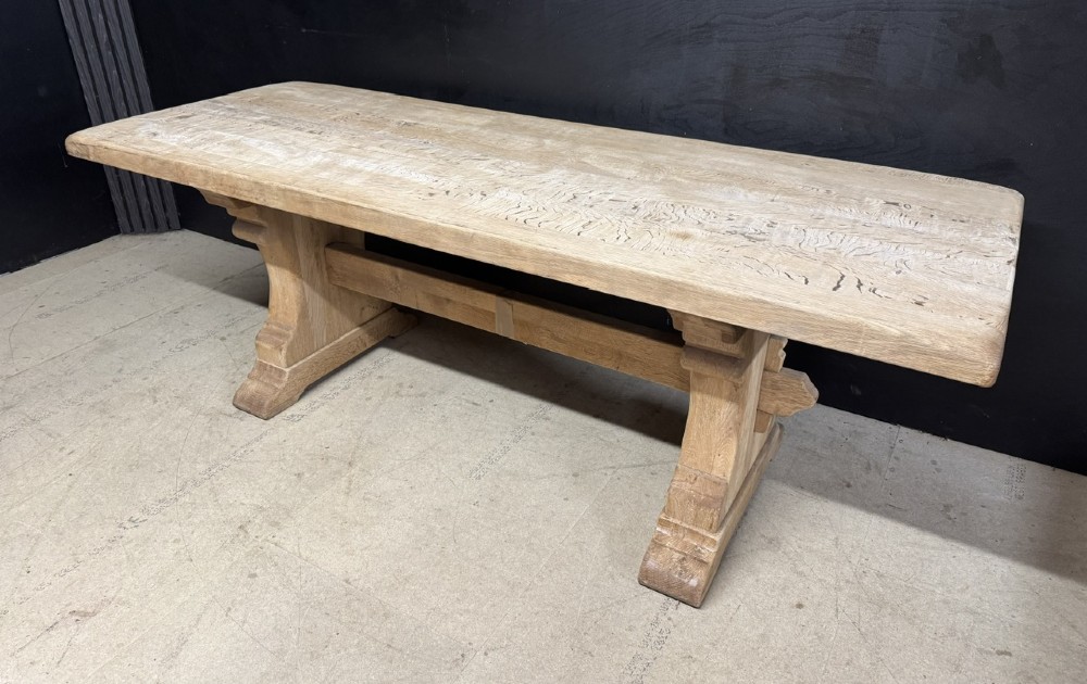 A rectangular bleached oak farmhouse dining table featuring a thick timber top supported by carved trestle legs and a central stretcher. View III