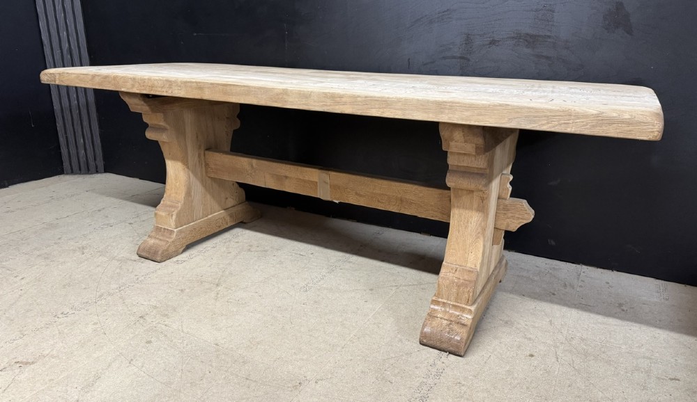 A rectangular bleached oak farmhouse dining table featuring a thick timber top supported by carved trestle legs and a central stretcher. View IV