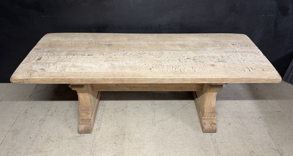 A rectangular bleached oak farmhouse dining table featuring a thick timber top supported by carved trestle legs and a central stretcher. View VIII