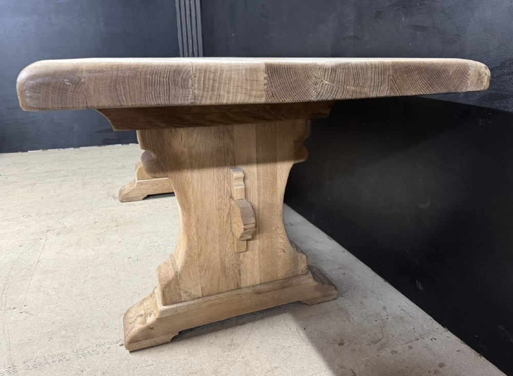A rectangular bleached oak farmhouse dining table featuring a thick timber top supported by carved trestle legs and a central stretcher. View IX